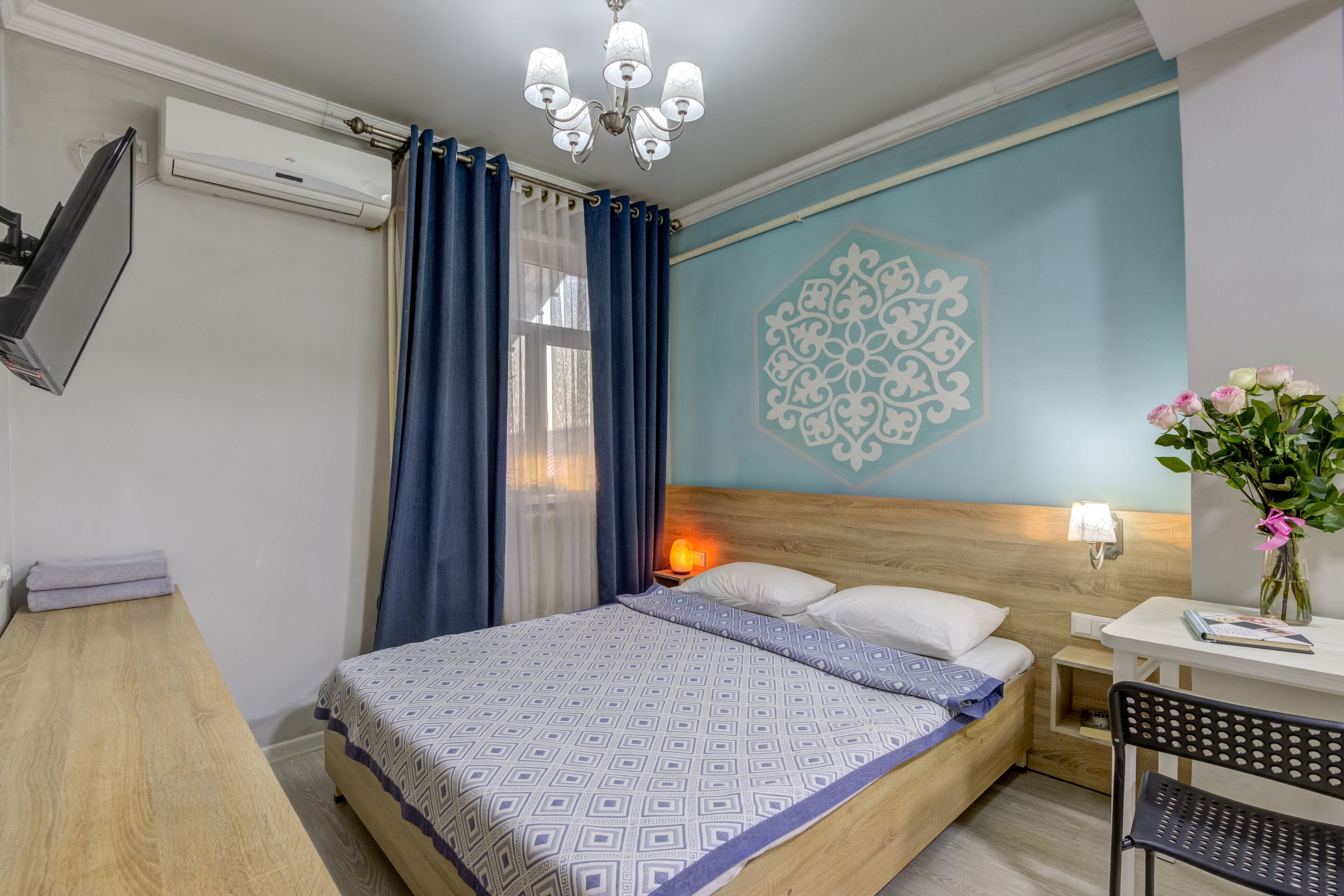 A bedroom with a bed, bedside table, lamp, and a wall decoration.