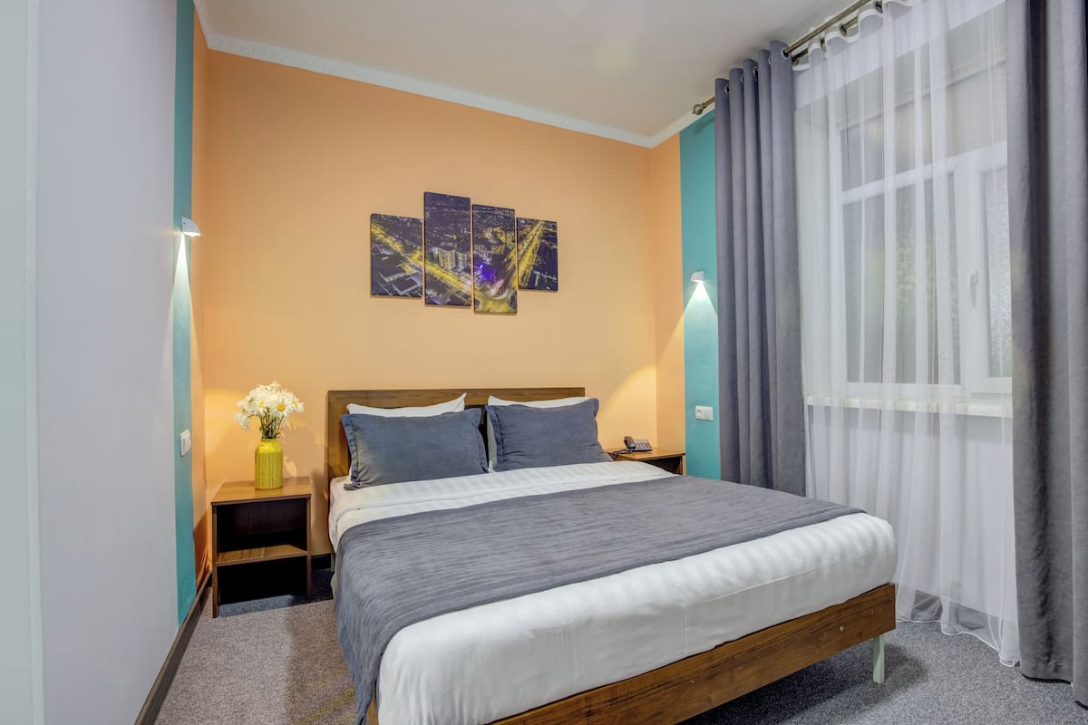 Un dormitorio ordenado con una cama grande, una mesita de noche con un florero y una obra de arte colgada en la pared.