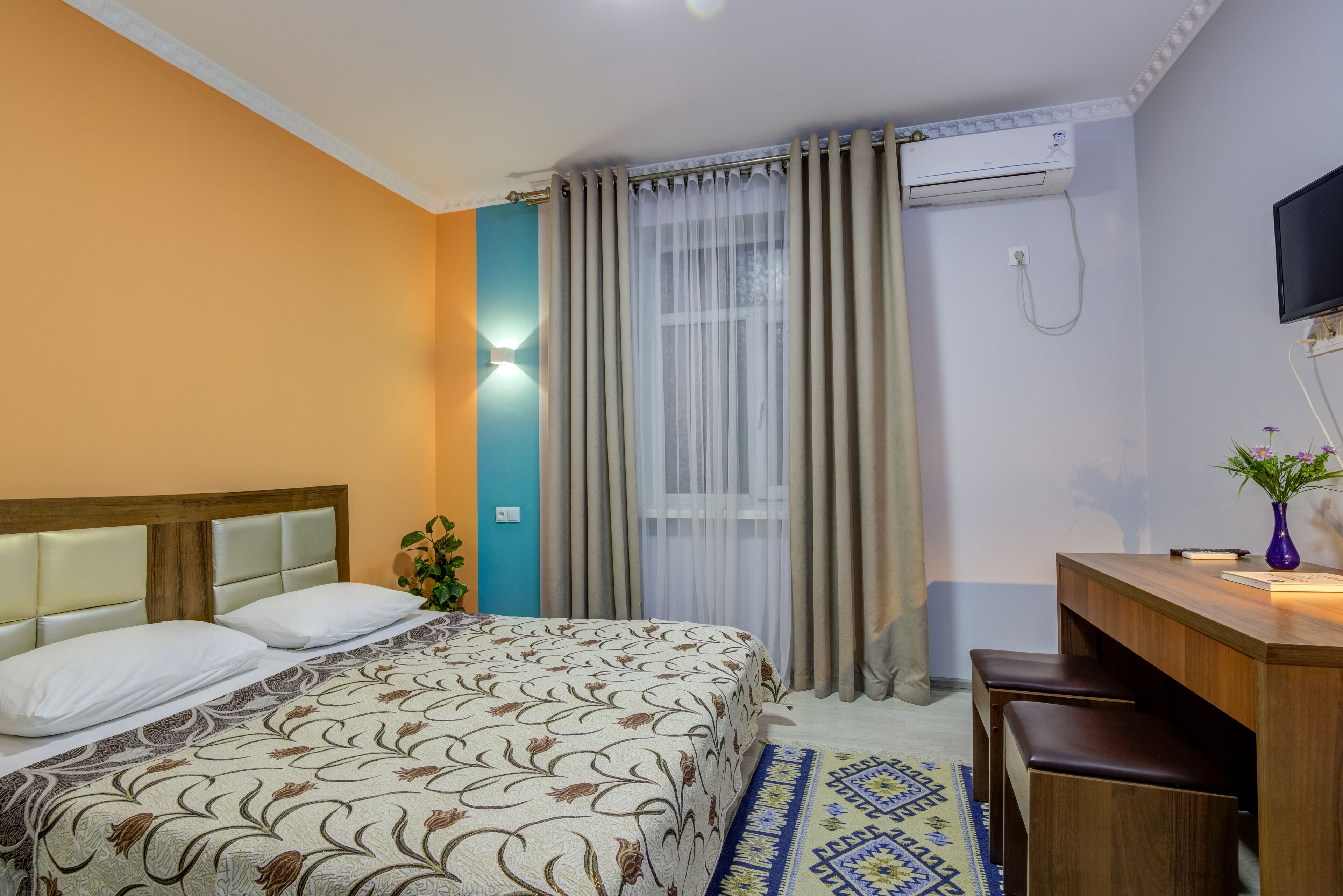 Habitación de hotel con cama, escritorio, silla, televisor y ventana con cortinas.