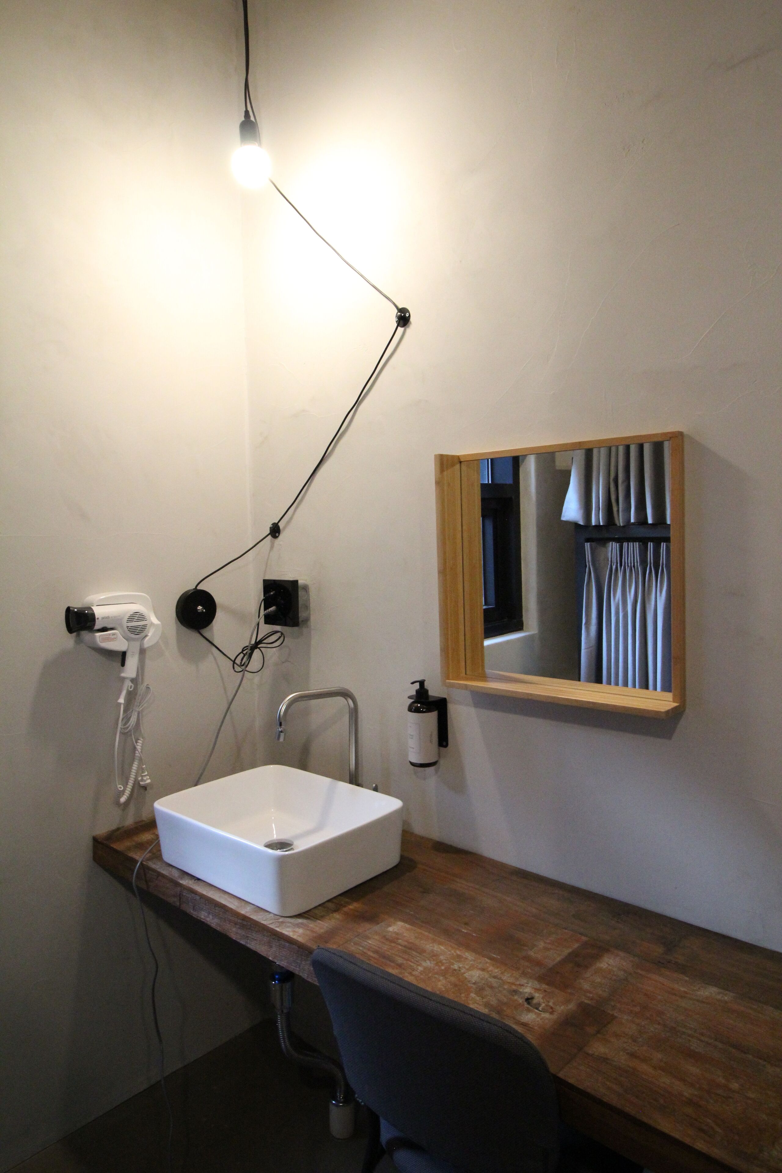 A bathroom with a wooden vanity, a white sink, a mirror, a hairdryer, and a light fixture.