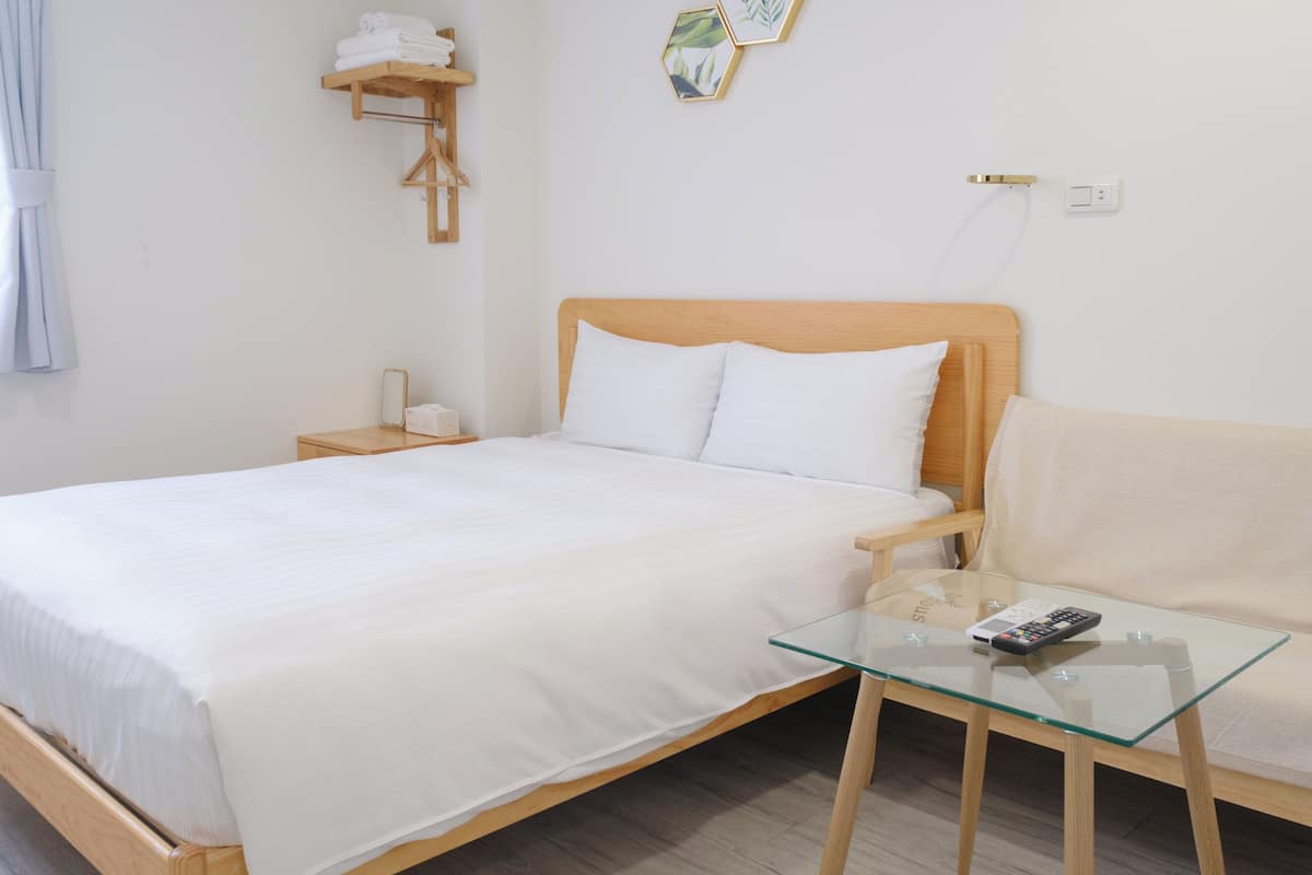 Un lit bien fait, avec du linge de lit blanc, une table de chevet avec une lampe et une table basse en verre avec une télécommande.