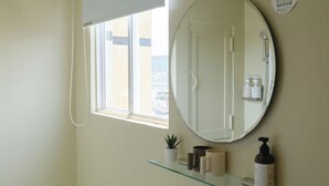 A bathroom with a round mirror, a potted plant, and toiletries on a glass shelf. - See U Apartment (Tainan)