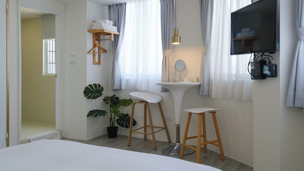A modern hotel room with a bed, a vanity with a mirror, a television mounted on the wall, and a potted plant. - See U Apartment (Tainan)