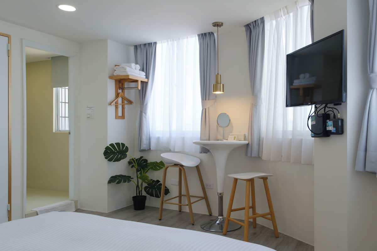 Une chambre d’hôtel moderne, équipée d’un lit, d’une coiffeuse avec un miroir, d’un téléviseur fixé au mur et d’une plante en pot.
