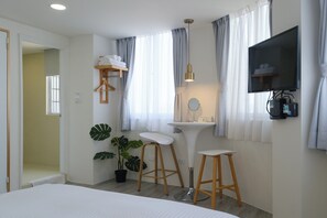 A modern hotel room with a bed, a vanity with a mirror, a television mounted on the wall, and a potted plant. - See U Apartment (Tainan)