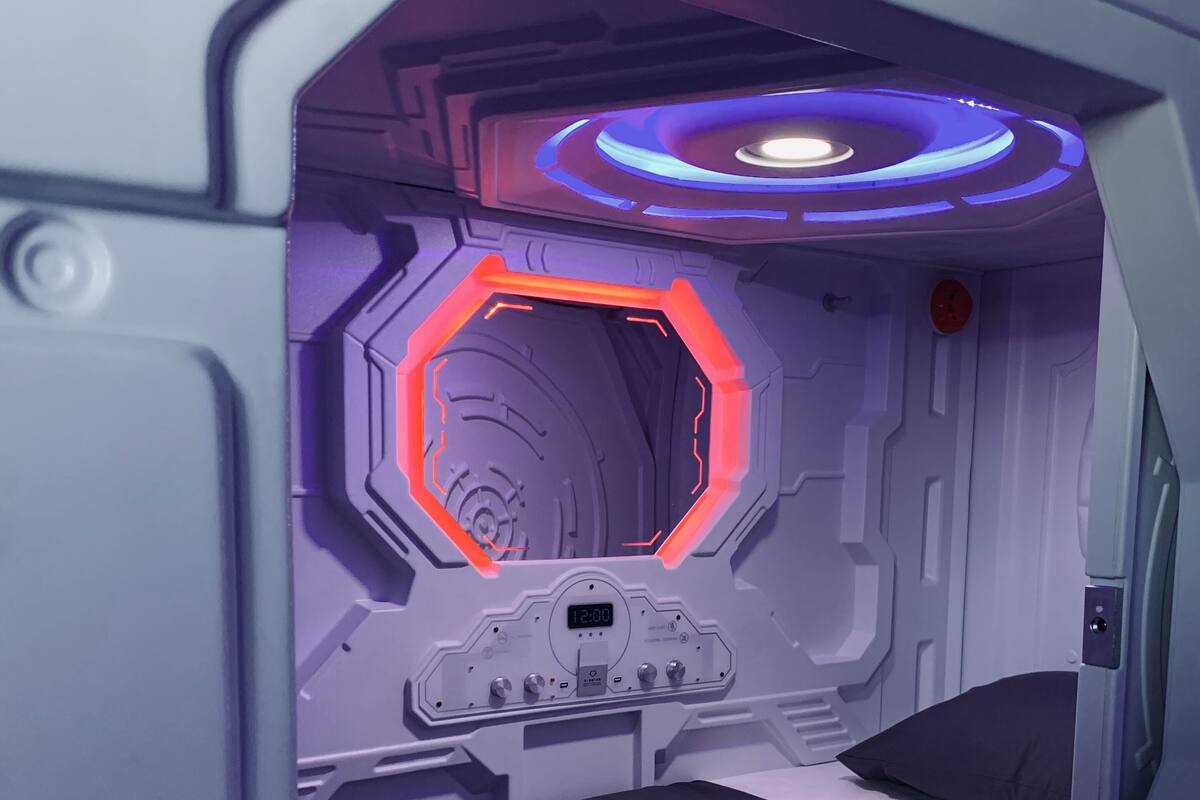 A futuristic room with a hexagonal window, a control panel, and a bed.