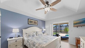 Un dormitorio con cama, mesita de noche, lámpara, ventilador de techo y vista a una piscina a través de un ventanal.