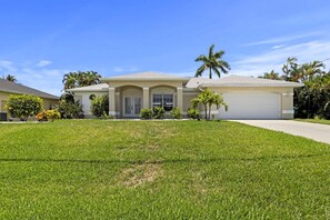 A single-story house with a garage, surrounded by a well-maintained lawn and palm trees.