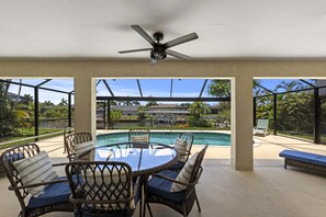 A covered outdoor area with a pool, wicker furniture, and a ceiling fan.