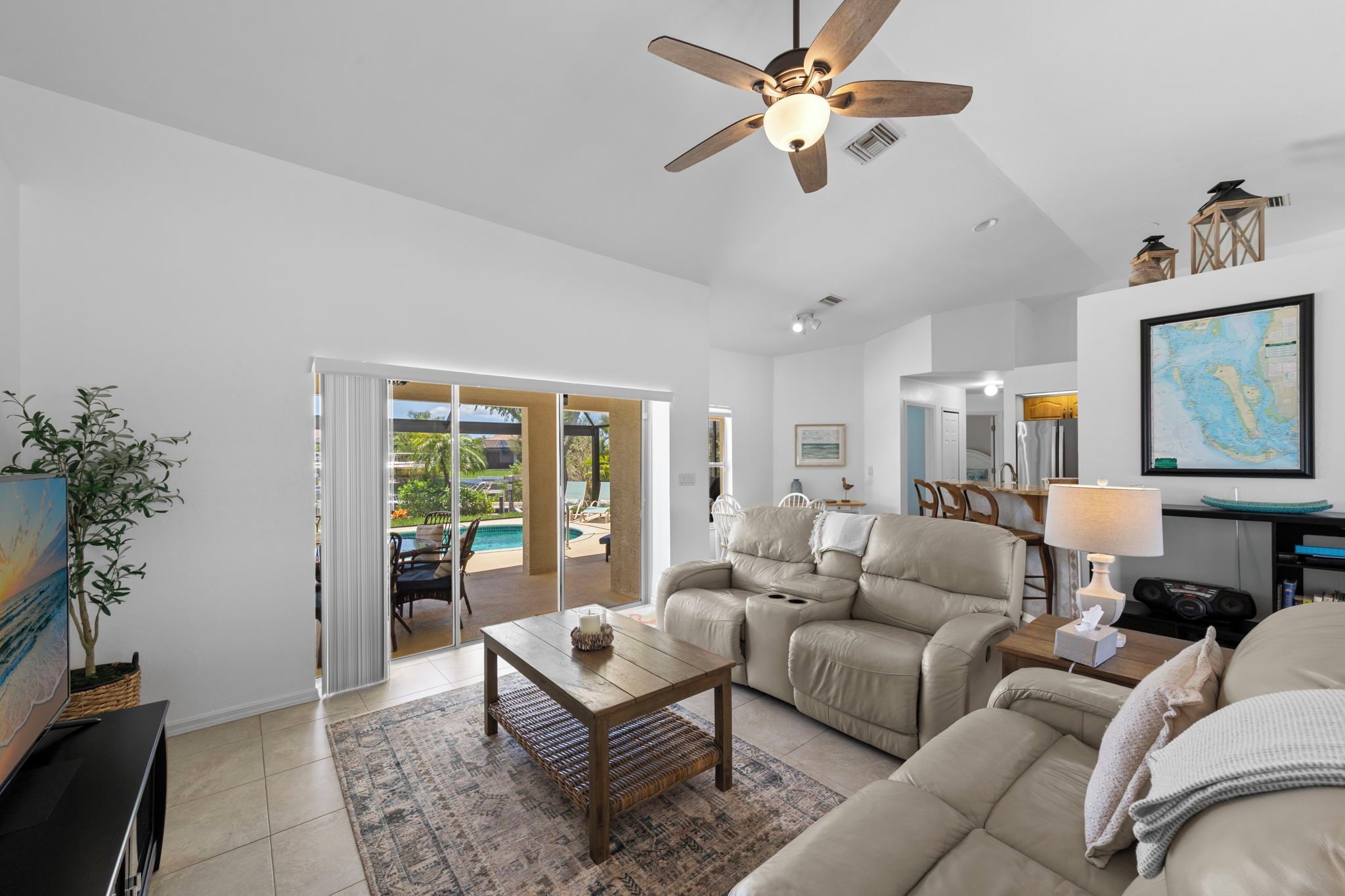 A spacious living room with a ceiling fan, a sofa set, a coffee table, and a view of a pool through glass doors.