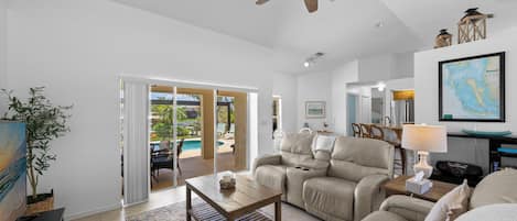 A spacious living room with a ceiling fan, a sofa set, a coffee table, and a view of a pool through glass doors.