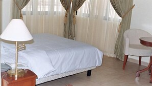 A hotel room with a bed, a bedside lamp, a chair, and curtains. - Eeyilobe Guest House (Lagos)
