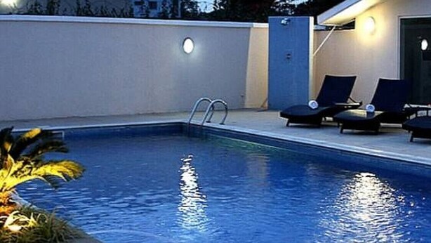 A swimming pool with a ladder, lounge chairs, and a wall-mounted light fixture. - Eeyilobe Guest House (Lagos)