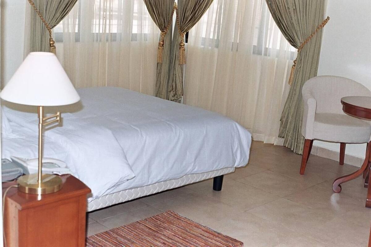 A hotel room with a bed, a bedside lamp, a chair, and curtains.