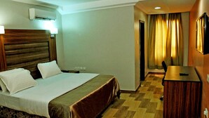 A hotel room with a bed, a nightstand, an air conditioning unit, a desk, and a chair. - Dmatel Hotel and Resort (Lekki)