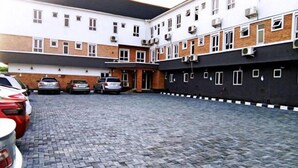 A multi-story building with a brick facade, a paved courtyard, and several parked cars. - Dmatel Hotel and Resort (Lekki)