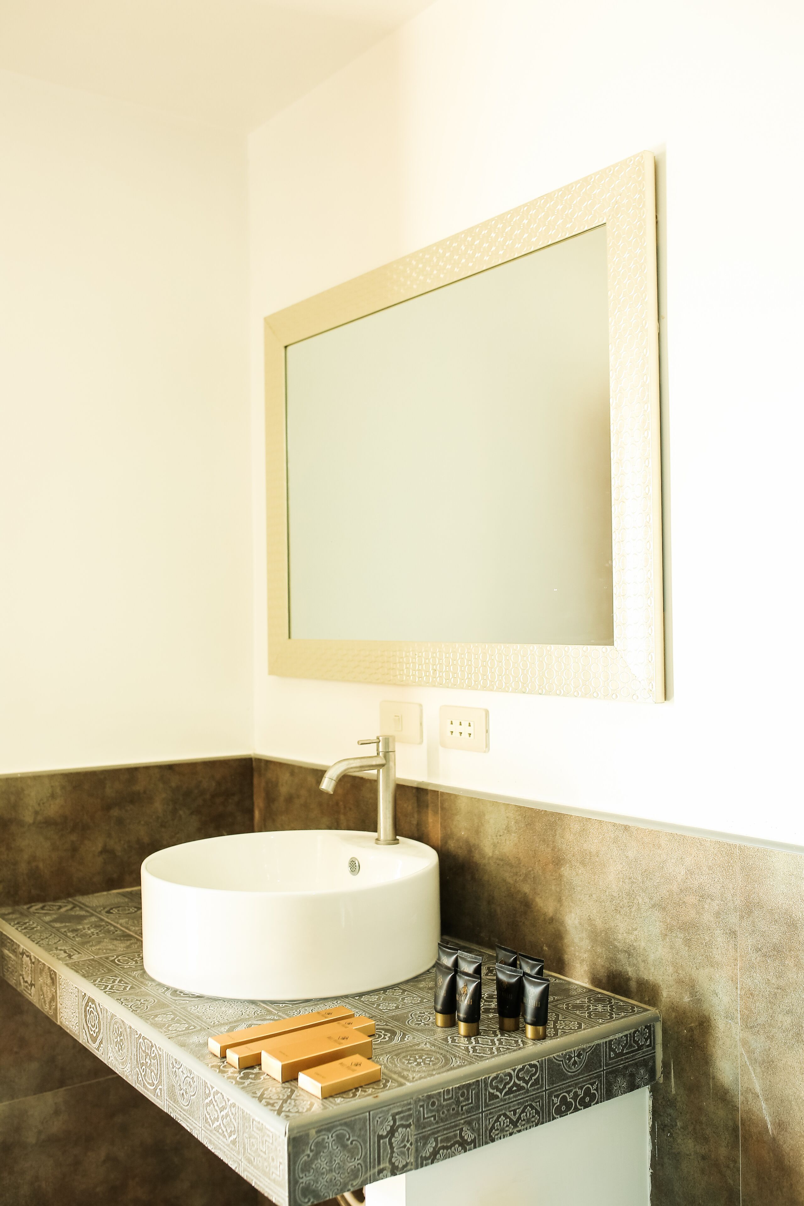 A bathroom with a white sink, a mirror, and a patterned countertop.