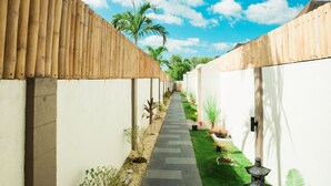 A pathway flanked by white walls and bamboo fences, leading to a building with a tiled roof.
