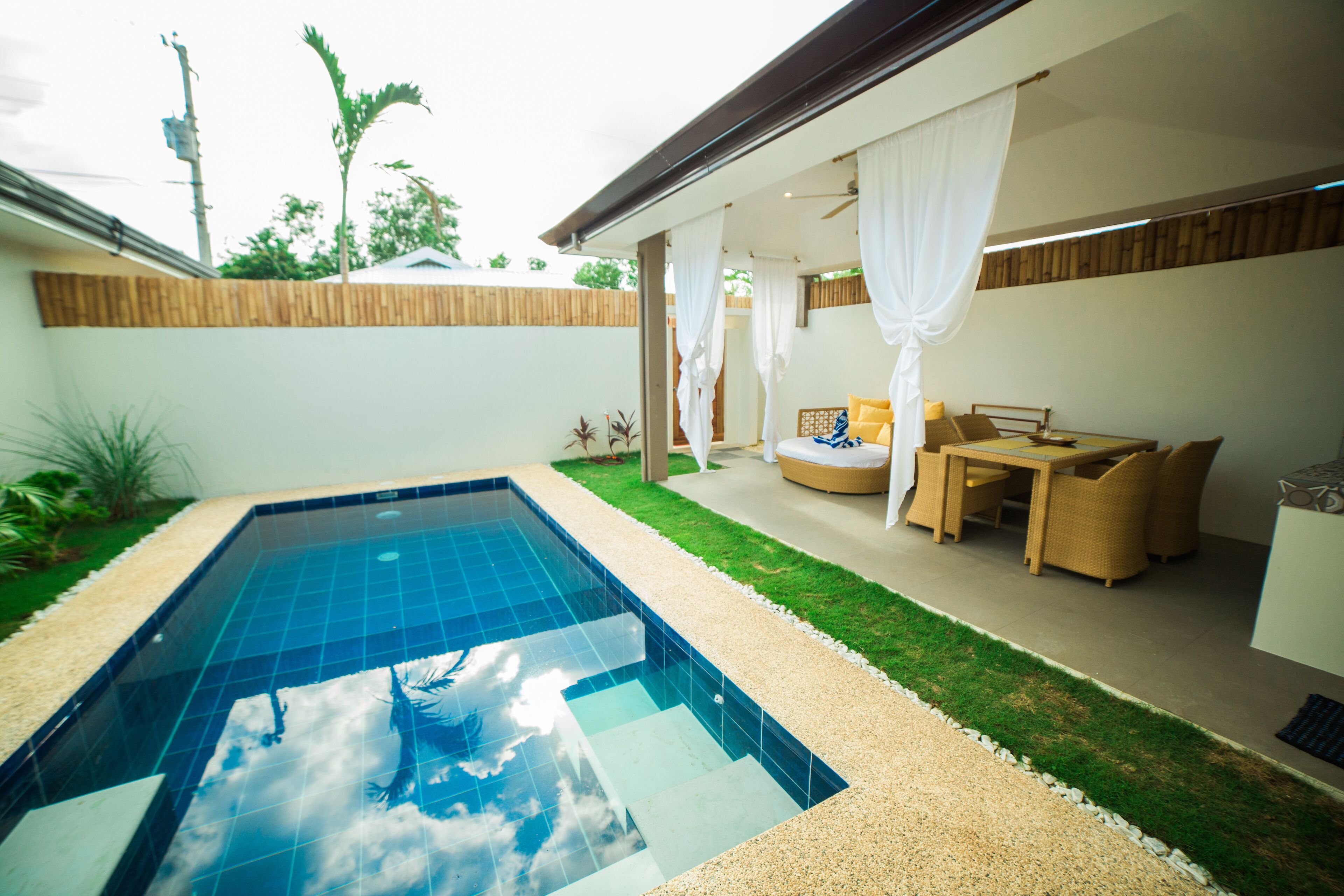 Una piscina con superficie de agua azul cristalina, rodeada por un césped bien cuidado y una zona de patio con mobiliario exterior.