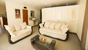 A living room with two white sofas, a glass coffee table with a vase, and wall art.