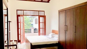 A bedroom with a bed, wooden wardrobe, and a view through a wooden door. - Villa304 (Galle)