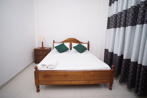 A neatly made bed with a wooden headboard, a nightstand with a lamp, and patterned curtains. - Villa304 (Galle)