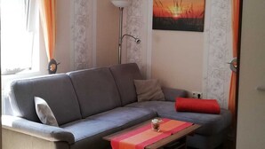 A living room with a sofa, a coffee table, a bed, and a painting on the wall.