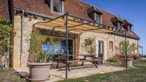 Een stenen huis met een overdekte patio, buitenmeubilair en plantenpotten.