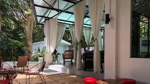 A covered outdoor seating area with wooden flooring, red cushioned stools, and wicker chairs. - Balconahe Resto Camp (Antipolo)