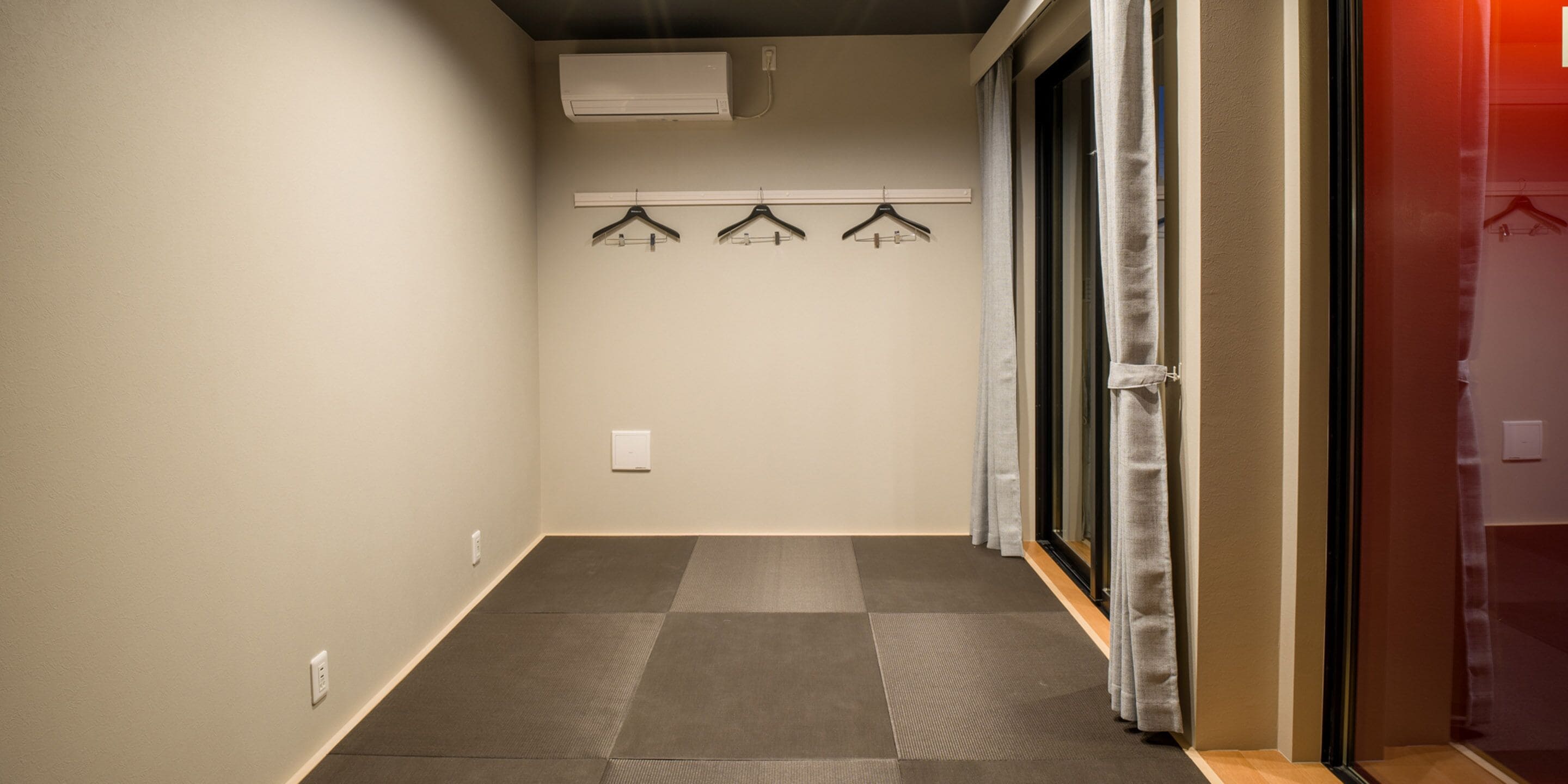 A hallway with a tiled floor, a wall-mounted air conditioner, and a set of three black hangers on a rod.
