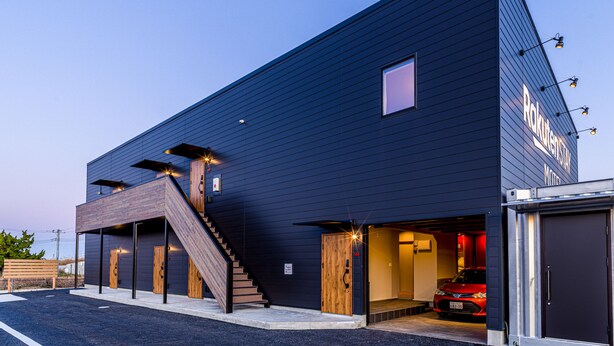 A modern building with a dark exterior, a wooden staircase, and a red car parked inside. - Rakuten STAY MOTEL Kujukurihama Katakai (Kujukuri)