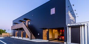 A modern building with a dark exterior, a wooden staircase, and a red car parked inside. - Rakuten STAY MOTEL Kujukurihama Katakai (Kujukuri)