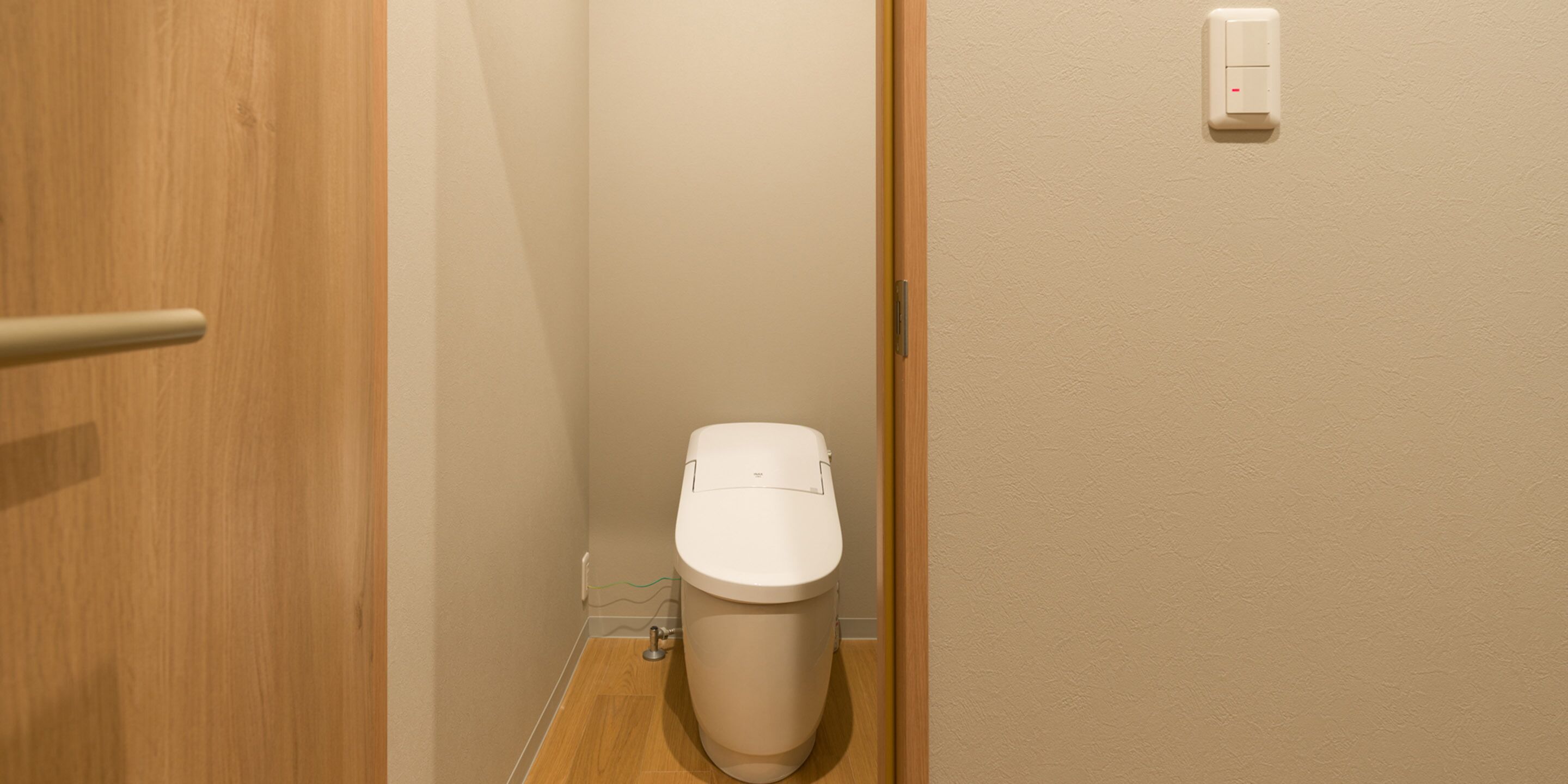Ein kleines, kompaktes Badezimmer mit Toilette, Holztür und einem an der Wand befestigten Lichtschalter.