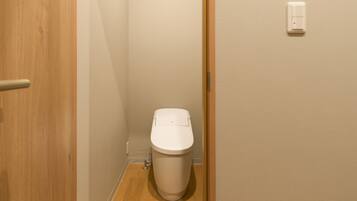 A small, compact bathroom with a toilet, wooden door, and a wall-mounted light switch.