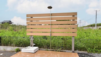 A bench with a water fountain in front of a fence with greenery.