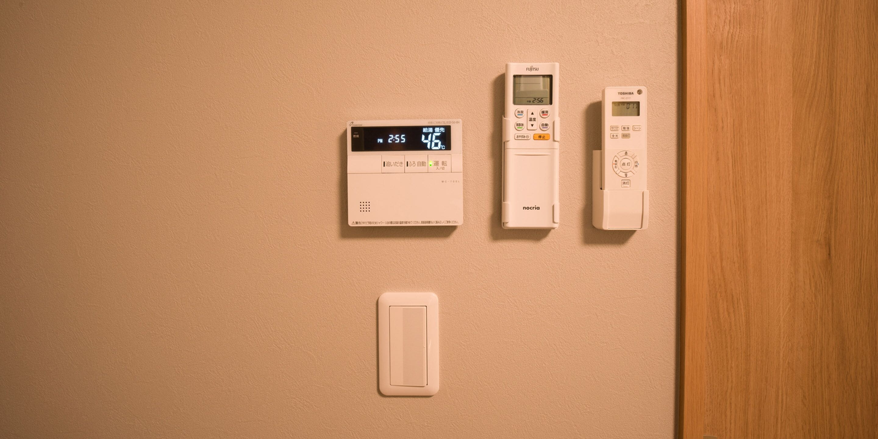 Tres termostatos y un interruptor de pared sobre una pared color beige.