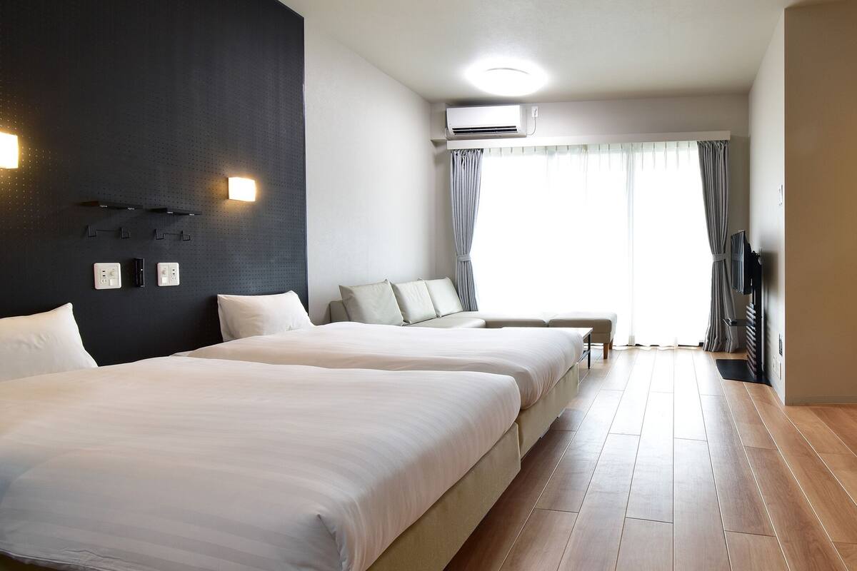 Ein Hotelzimmer mit zwei Betten, einem Schreibtisch, einem Spiegel und einem Badezimmer mit Waschbecken und Dusche.