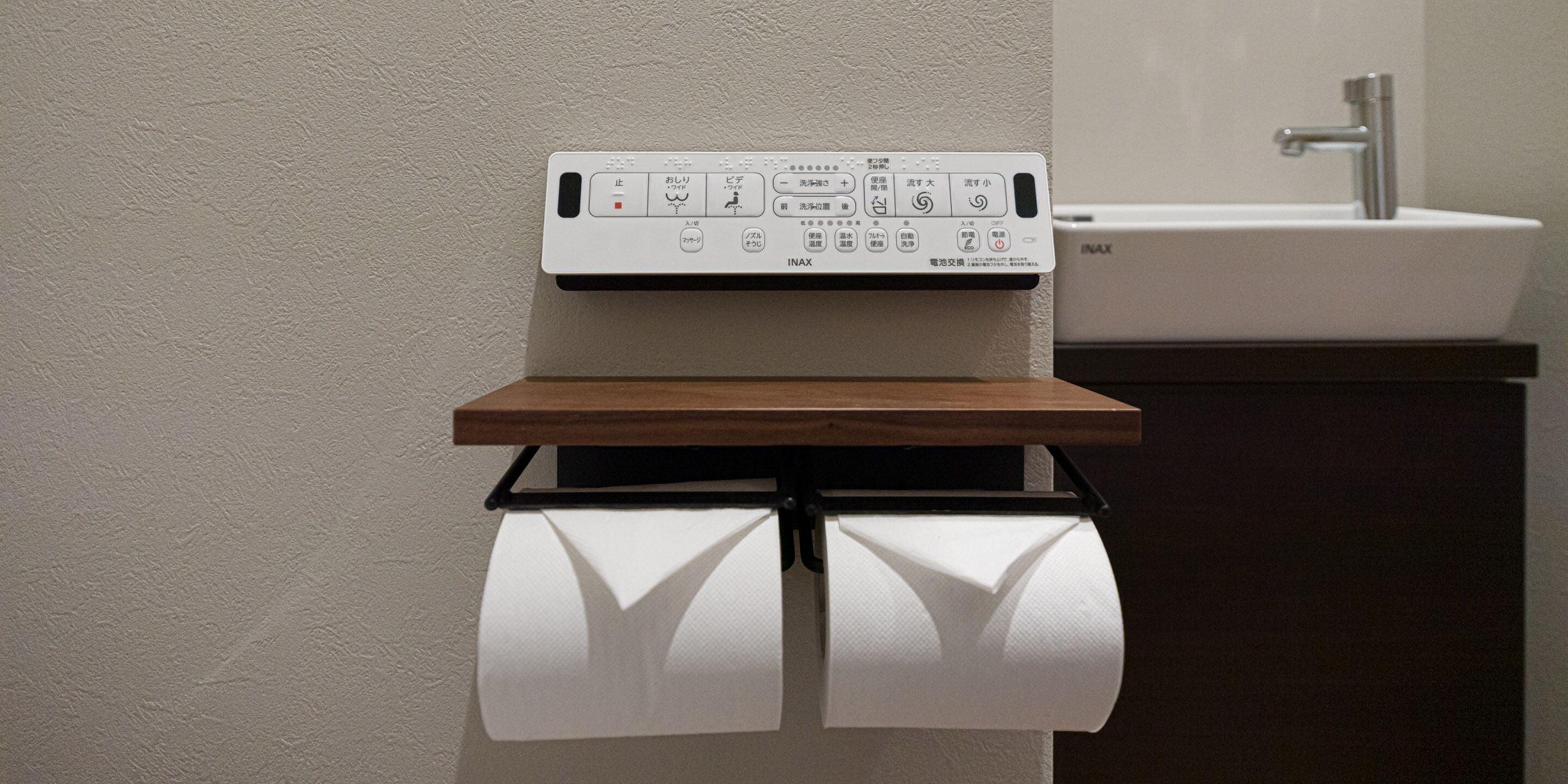A bathroom with a toilet paper holder, a sink, and a wooden shelf.