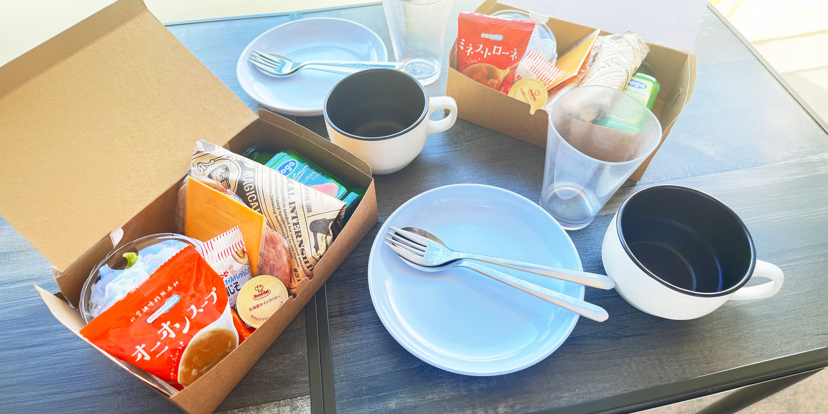 A table set with a white plate, a fork, a mug, and a box containing food items.
