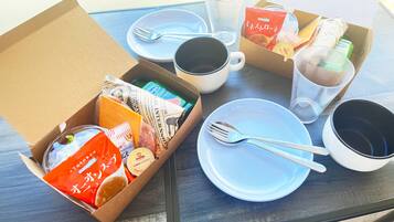 A table set with a white plate, a fork, a mug, and a box containing food items.