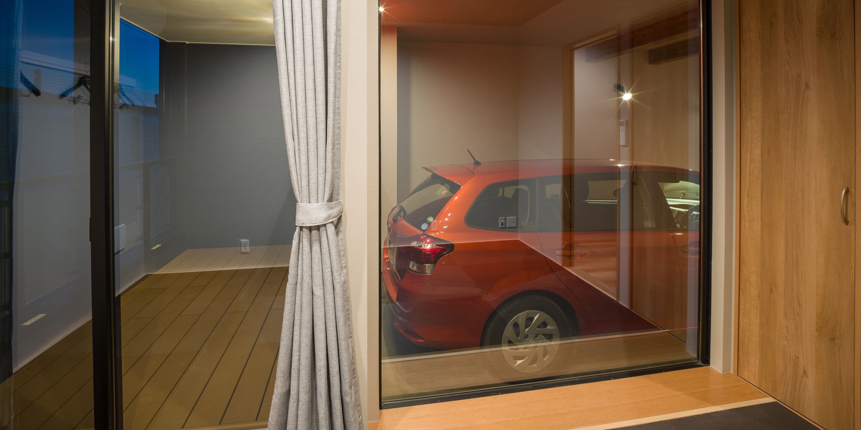 Ein modernes Zimmer mit Holzboden, einer Glastür, die ein rotes Auto reflektiert, und einem Vorhang.