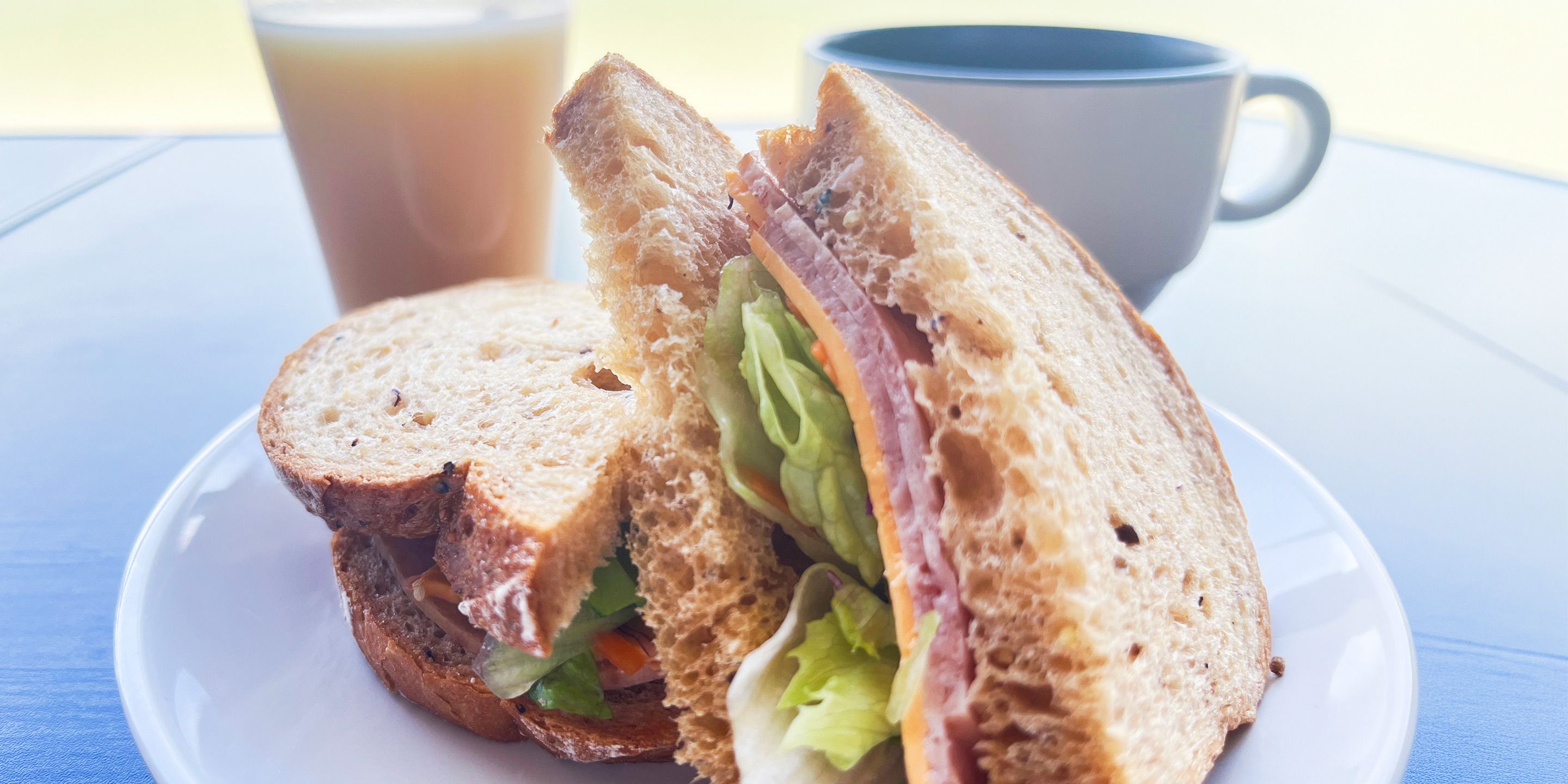A sandwich on a plate with a cup of beverage in the background.