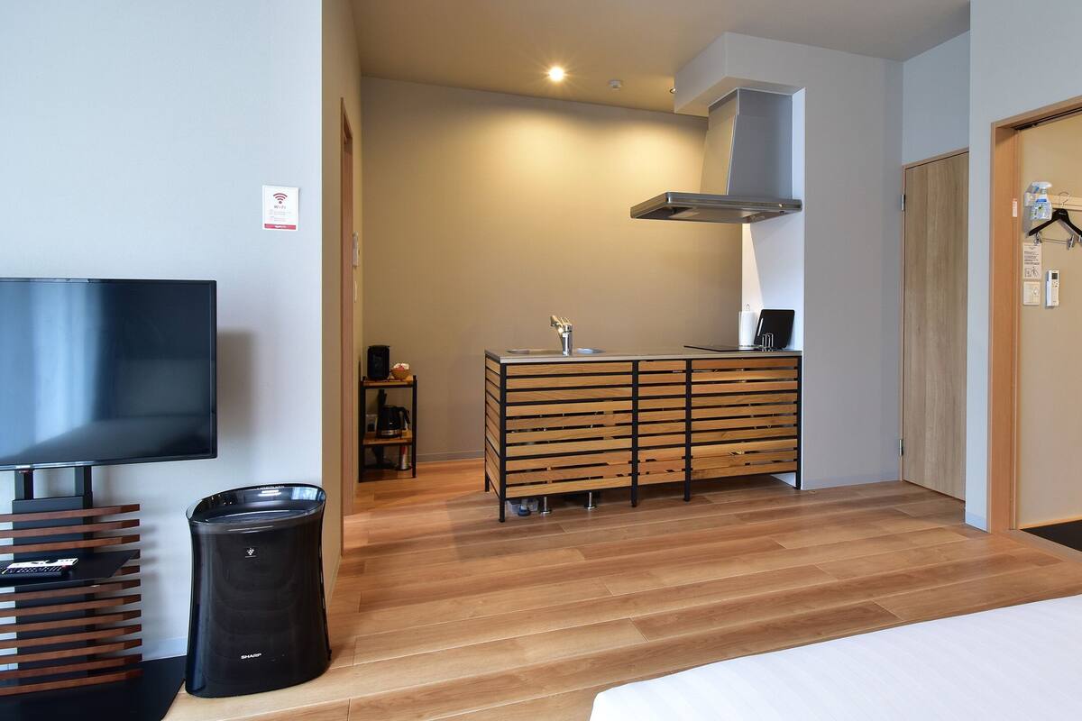 Ein modernes Hotelzimmer mit Flachbildfernseher, einem Holzkasten, einer schwarzen Mülltonne und einem Bett mit weißer Bettwäsche.