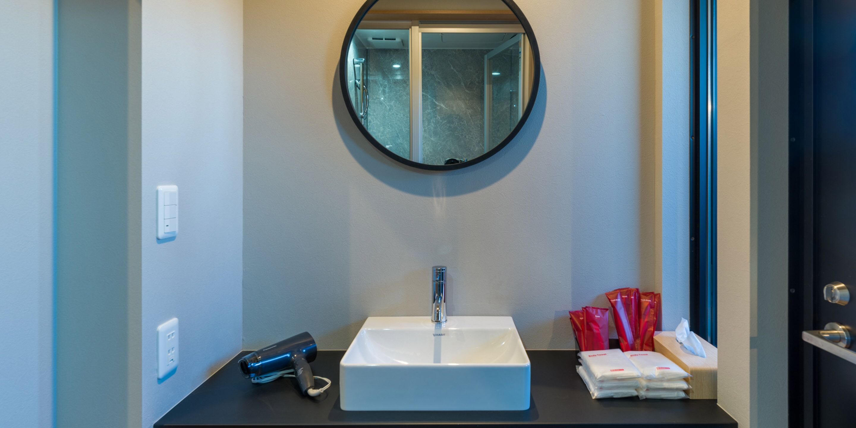 Un baño con un lavabo blanco, un espejo redondo y una encimera negra.