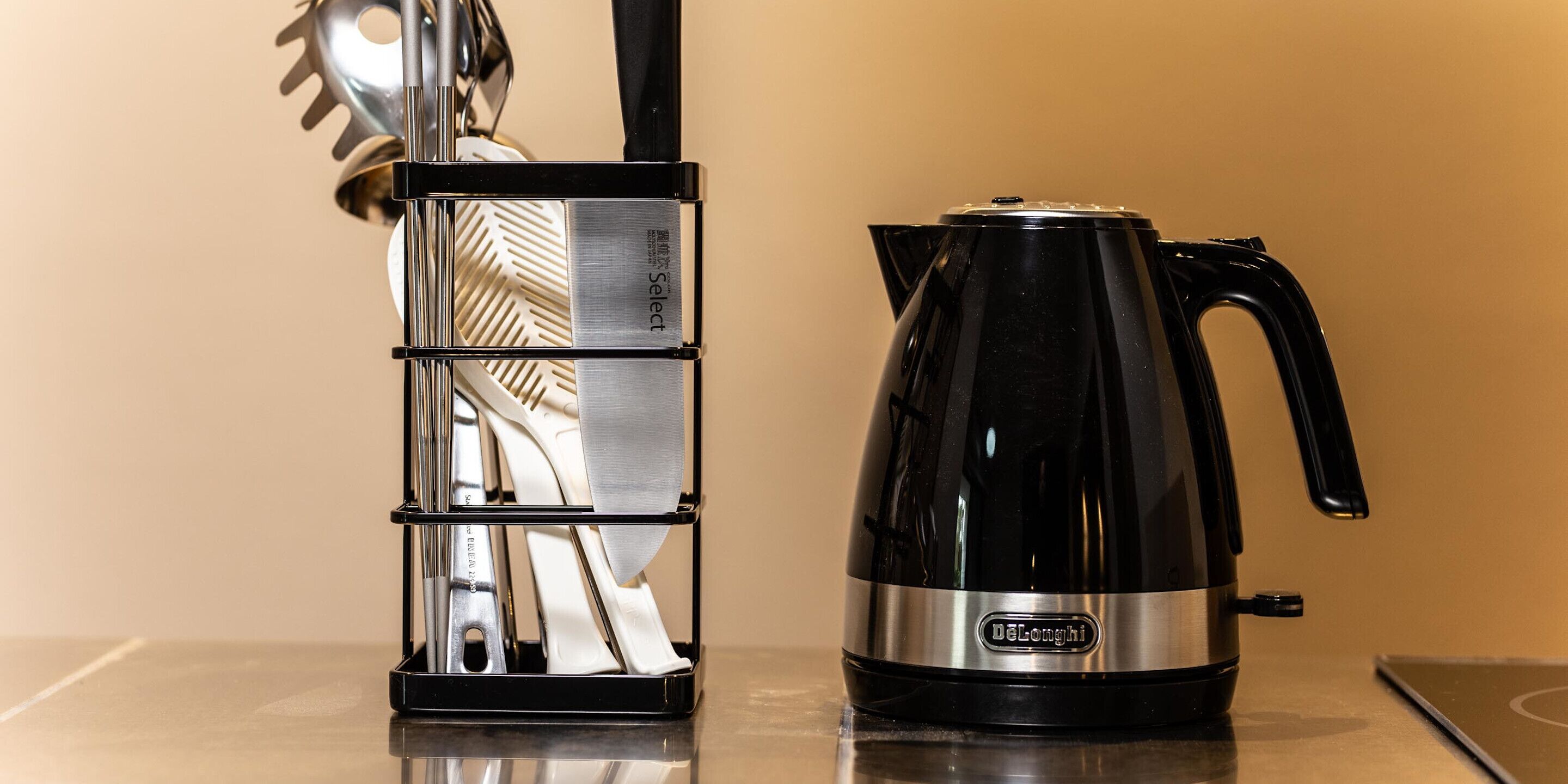 A black coffee maker and a stainless steel utensil holder on a reflective surface.