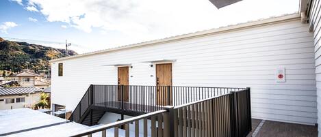 Un edificio blanco con puerta de madera, barandal negro y vista a un paisaje montañoso.