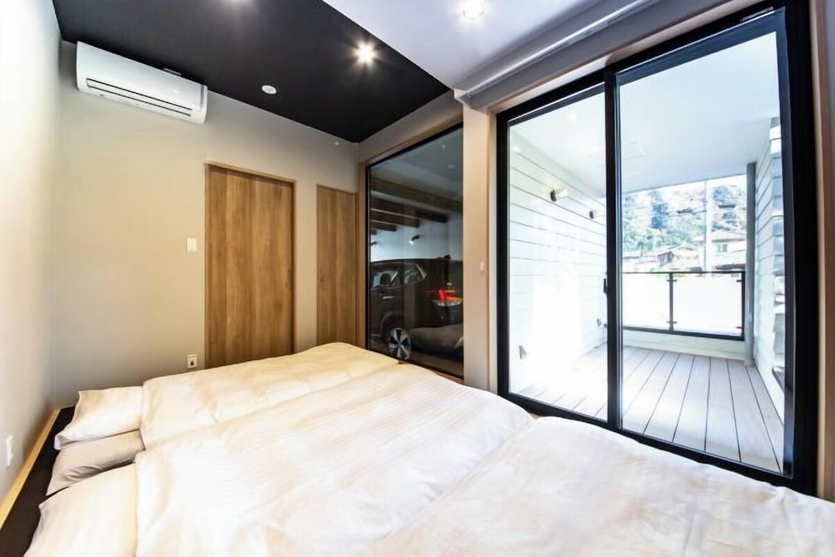 A bedroom with a large bed, sliding glass doors leading to a balcony, and a car parked outside.