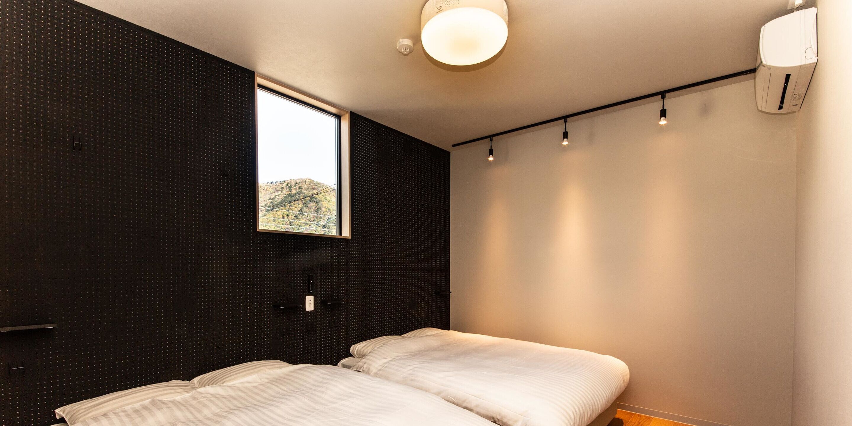 A modern bedroom with a large window, a bed, and a wall-mounted air conditioner.