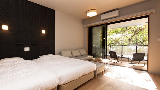 A modern bedroom with a large bed, a sofa, and a balcony with chairs.