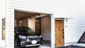 A black SUV parked in a garage attached to a white building with a wooden door and a staircase leading to the upper level.